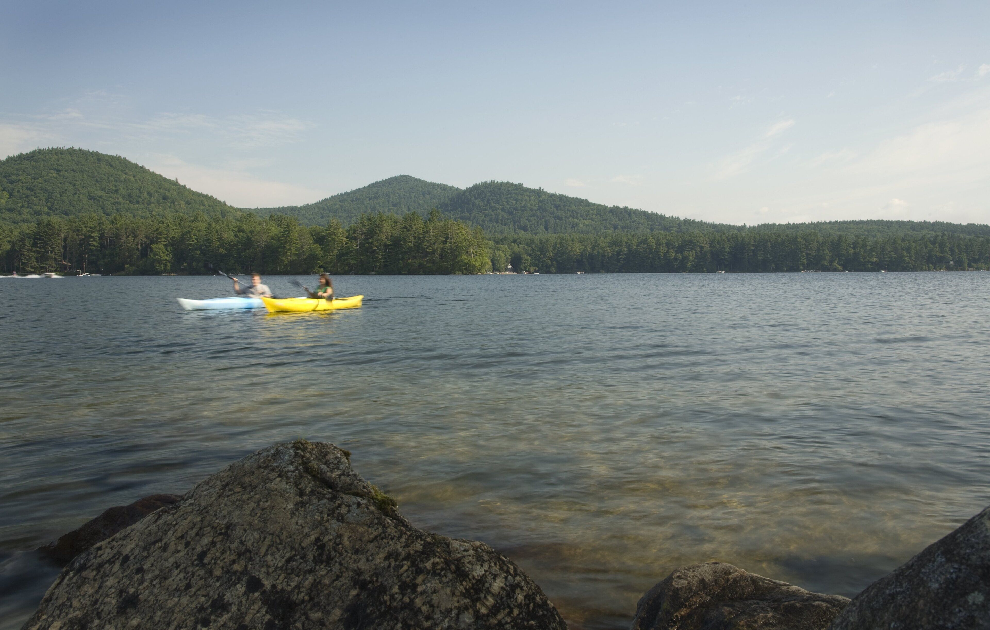 A calm lake with kayaks and a forested hill in the background.