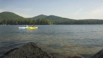 A calm lake with kayaks and a forested hill in the background.