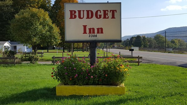 A sign for Budget Inn with the number 3306, surrounded by a flower bed and a grassy area with a road and trees in the background.