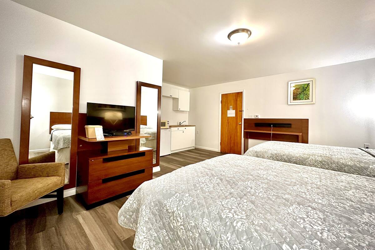 A hotel room with a bed, a TV, a desk, a chair, a microwave, and a door.