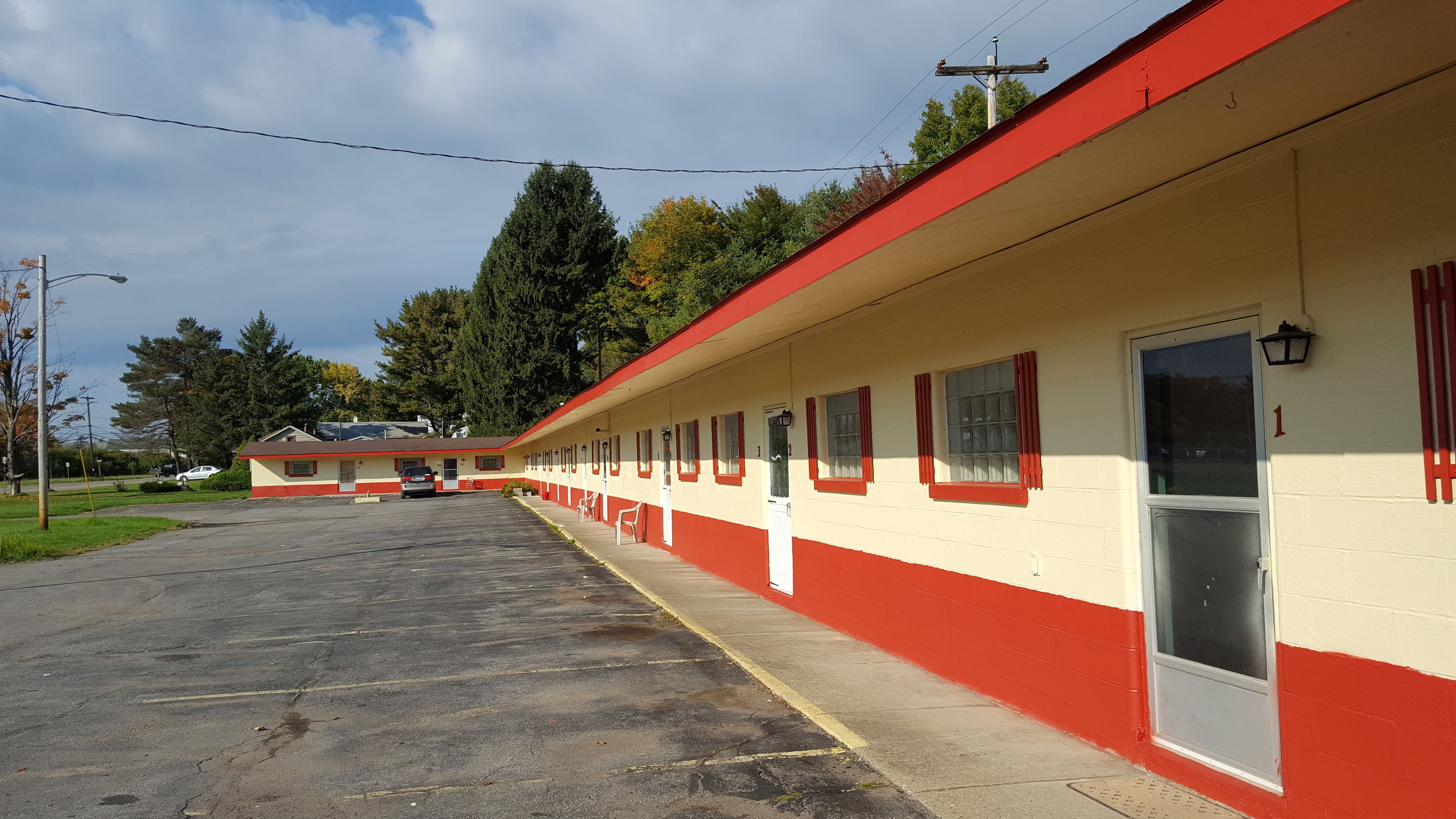 A motel with a row of rooms, a parking lot, and a building in the background.