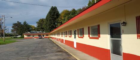 A motel with a row of rooms, a parking lot, and a building in the background.