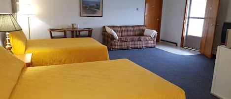 A room with two beds, a plaid sofa, a small table, and a television.