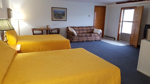 A room with two beds, a plaid sofa, a small table, and a television. - Crown Inn & Suites (Wellsville)