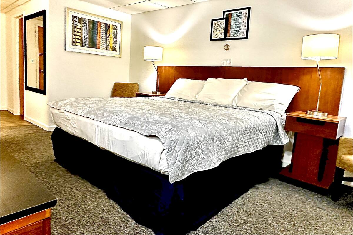 A hotel room with a large bed, two bedside lamps, a wooden headboard, and two framed artworks on the wall.