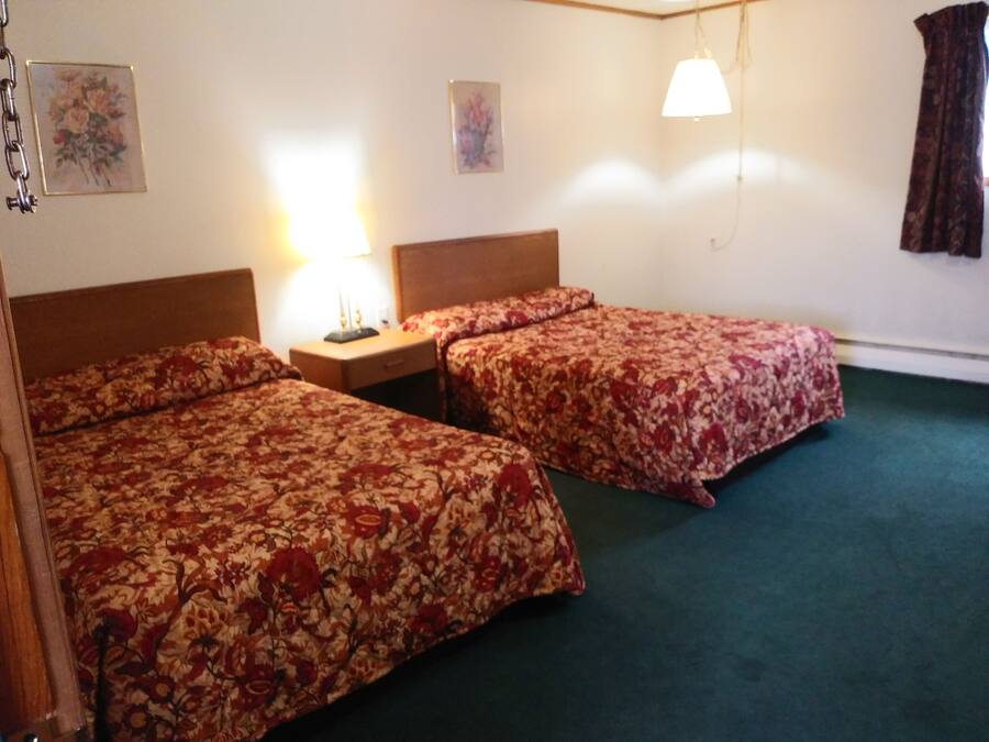 A hotel room with two beds, a nightstand, a lamp, and a hanging light fixture.