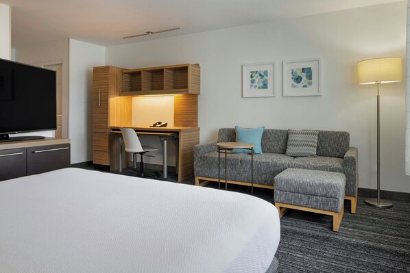 Une chambre d’hôtel avec un grand lit, un bureau avec une chaise, un canapé, une télévision et des œuvres d’art accrochées au mur.