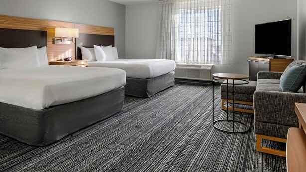 A hotel room with two beds, a sofa, a TV, and a small table.