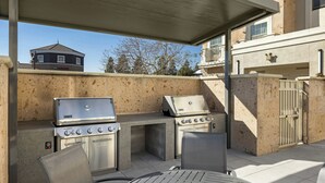 An outdoor patio with two stainless steel grills, a round table, and chairs.