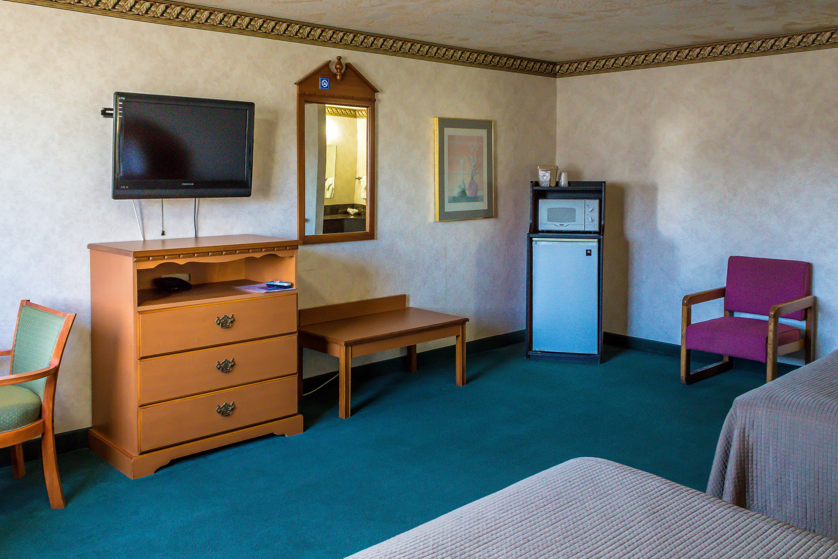 A hotel room with a television, a dresser, a desk, a chair, a microwave, and a framed picture on the wall.