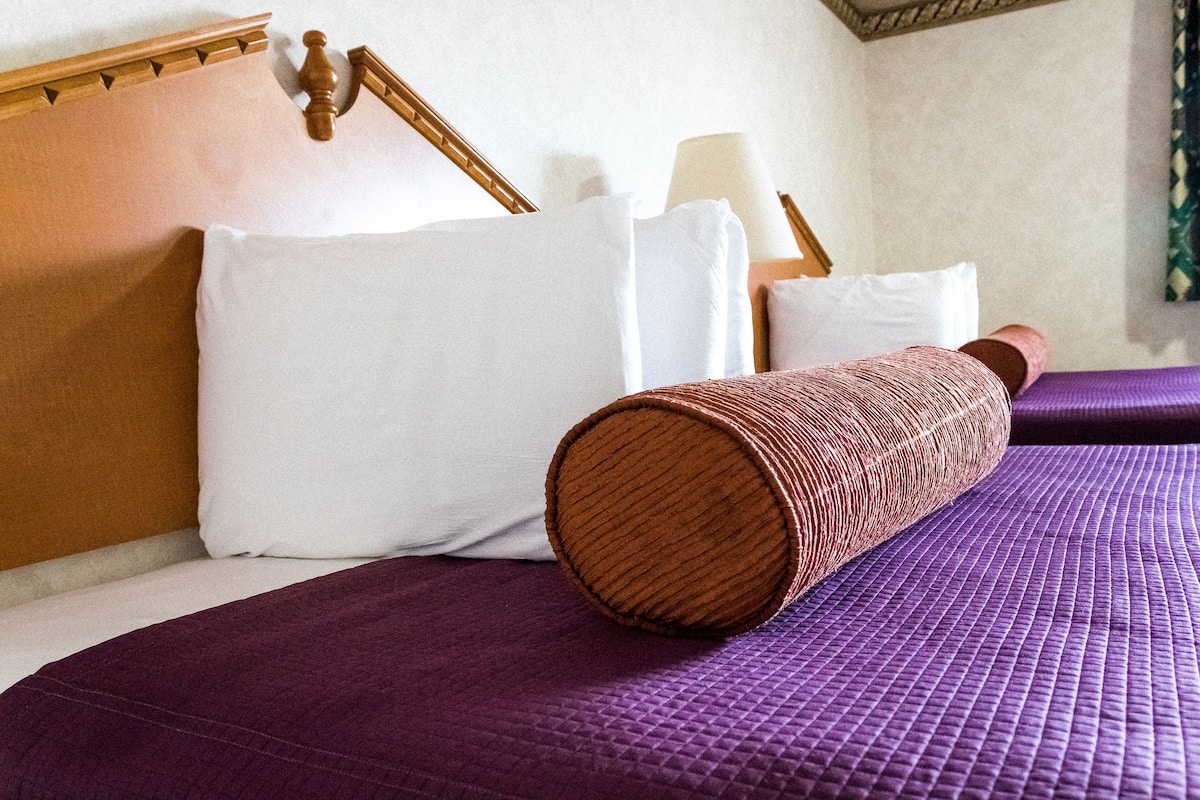 Ein Bett mit einer violetten gesteppten Decke, weißen Kissen und einem hölzernen Kopfteil.