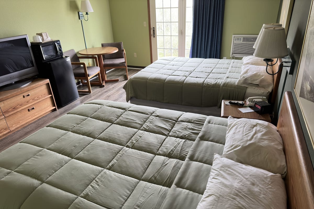 A hotel room with two beds, a TV, a desk, and a chair.