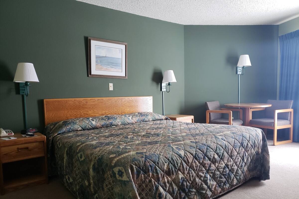 A hotel room with a large bed, two bedside tables, a desk with a chair, and two wall-mounted lamps.