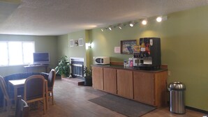 A compact kitchen with a microwave, coffee machine, and a trash can. There is a dining area with a table and chairs, and a television in the corner. - Harbor Lights Lodge (Kewaunee)