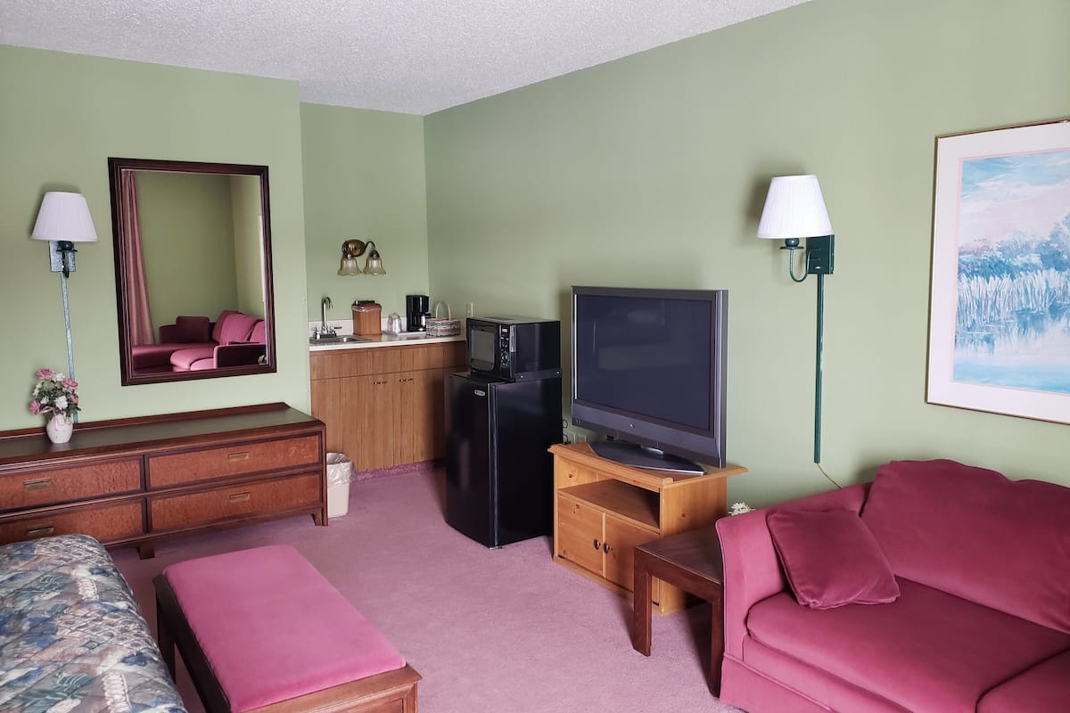 A compact living space with a kitchenette, a flat-screen TV, a sofa, a dining table, and a mirror.