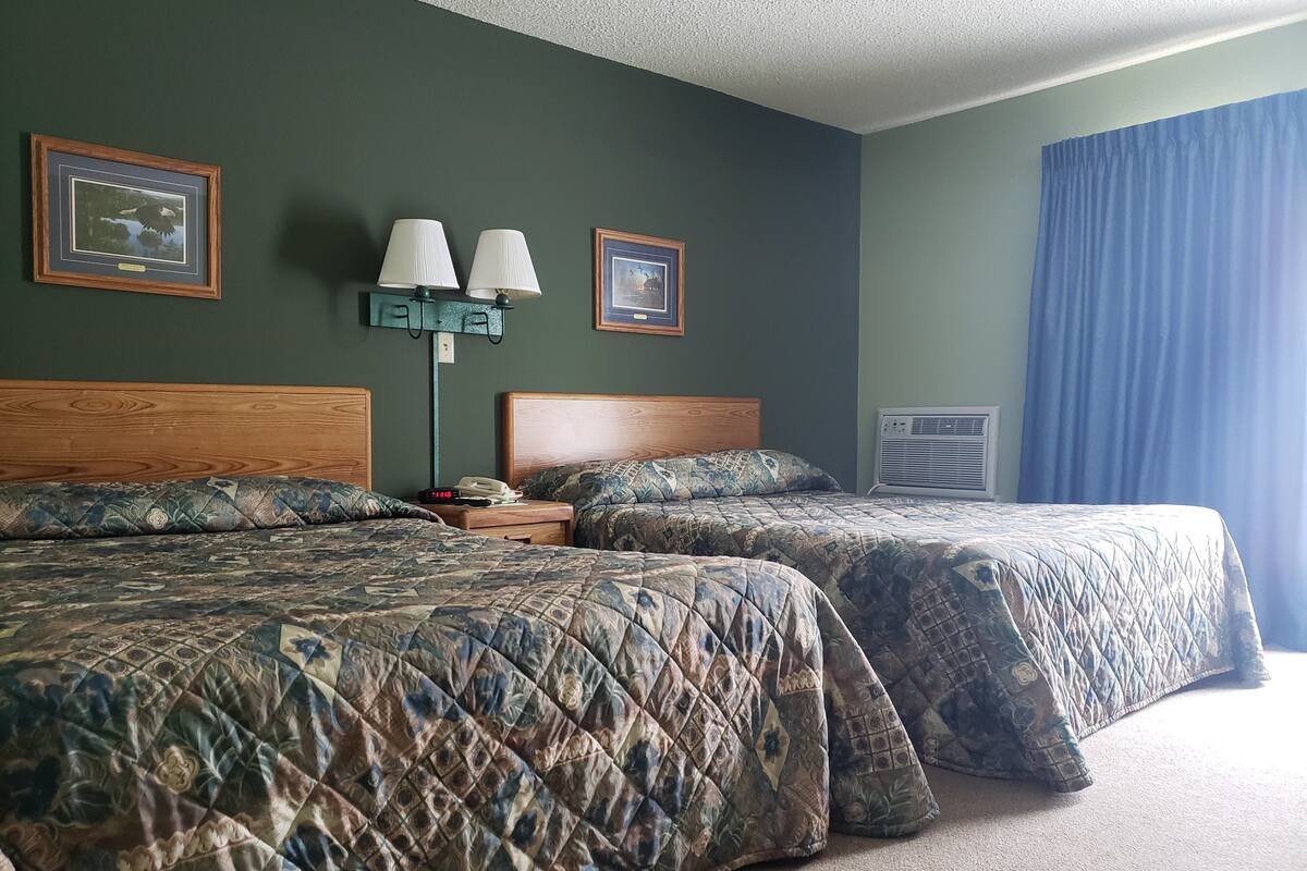 A hotel room with two beds, a nightstand, a lamp, and framed pictures on the wall.