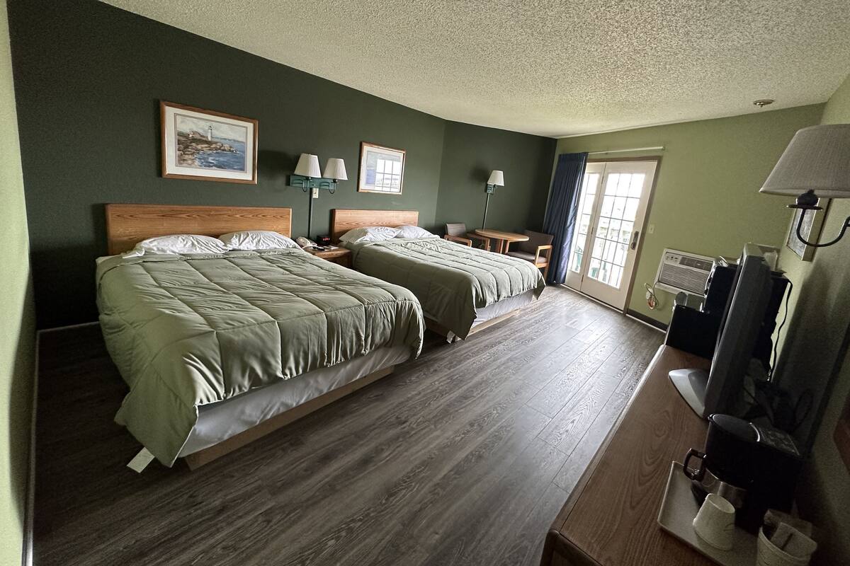A hotel room with two beds, a desk, a chair, a TV, and a window with curtains.
