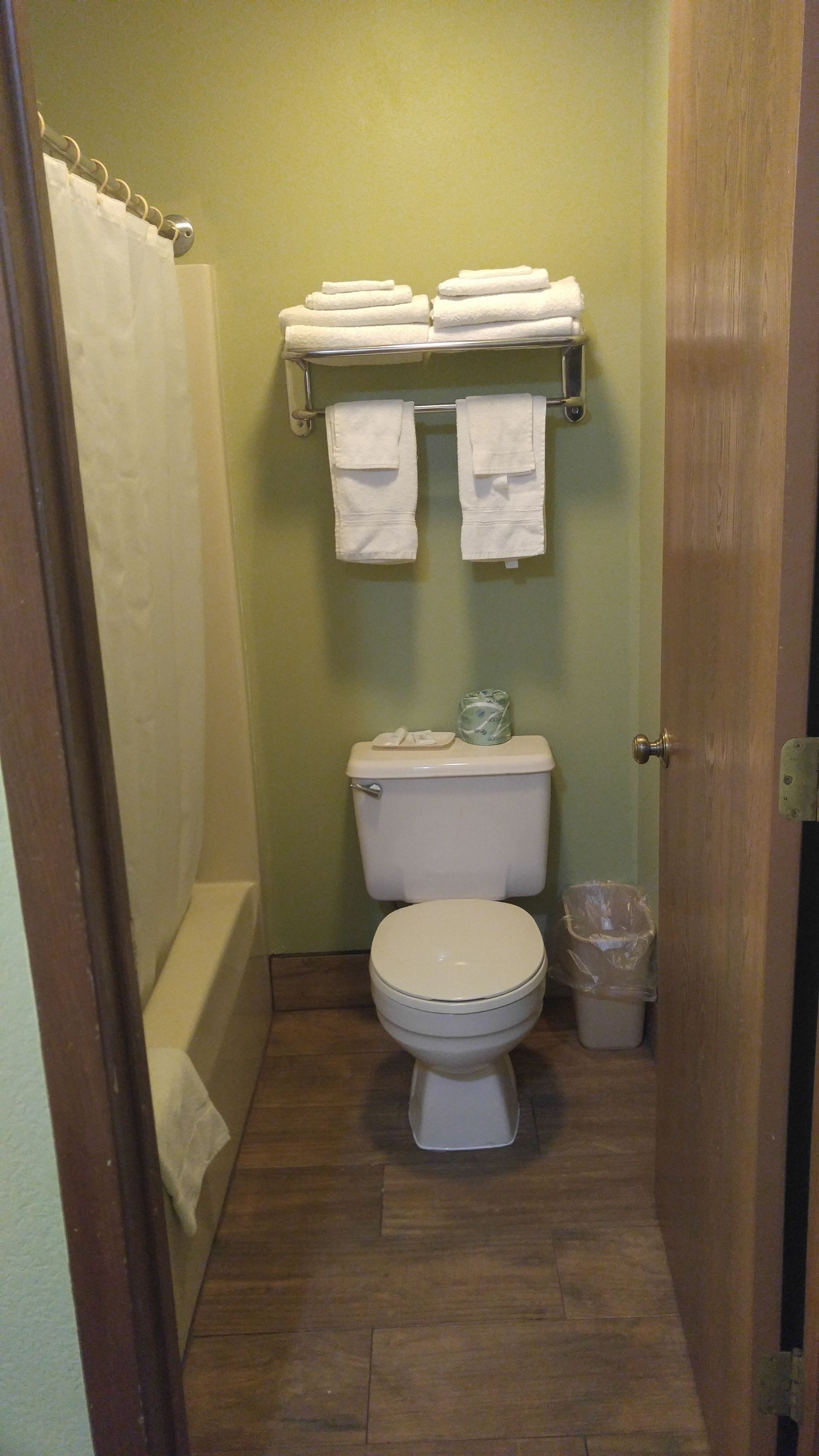 Une petite salle de bain comprenant des toilettes, un rideau de douche, un porte-serviettes avec des serviettes pliées et une poubelle.