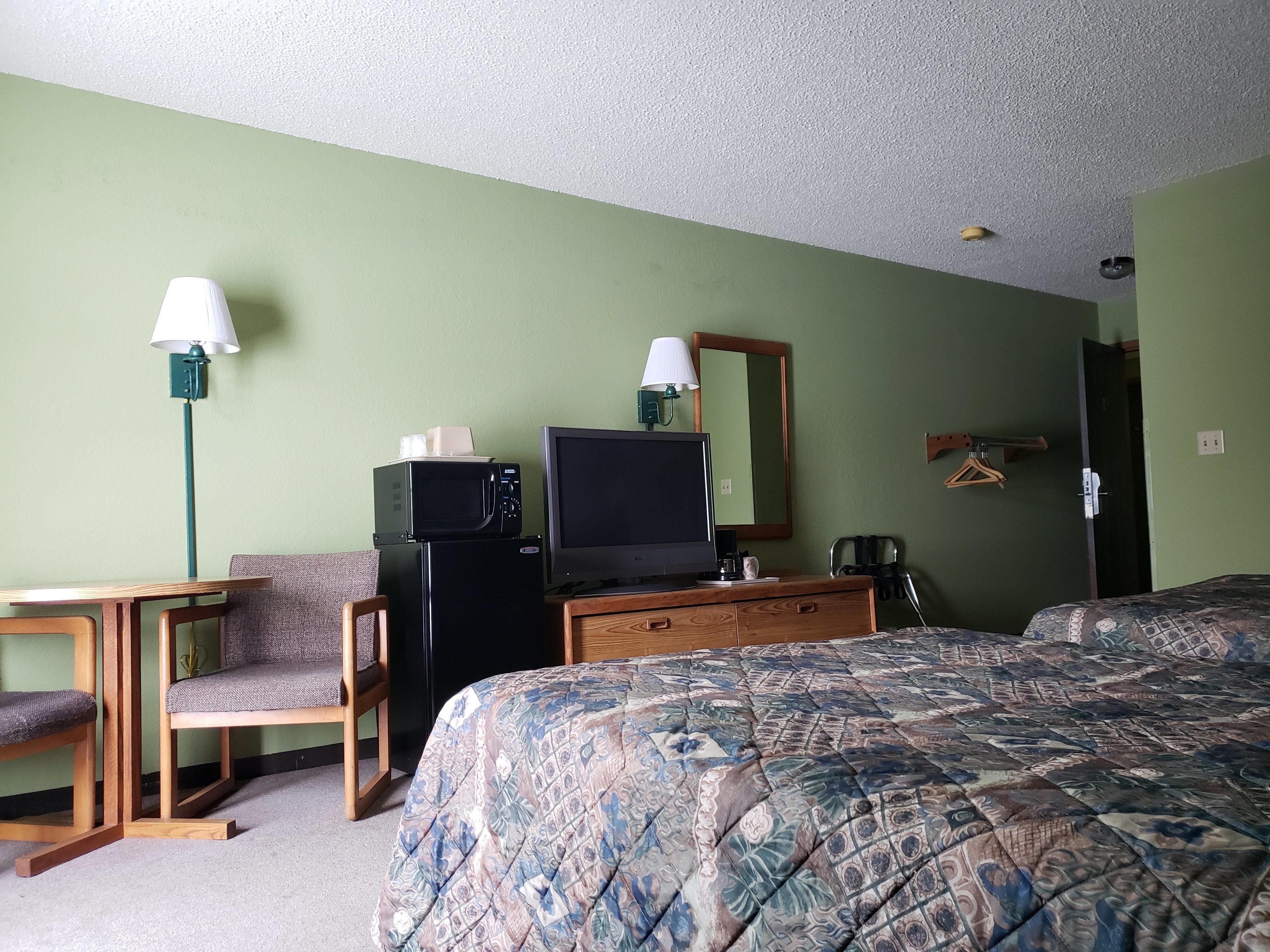 A hotel room with a bed, a desk, a chair, a television, a microwave, and a dresser.