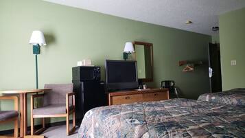 A hotel room with a bed, a desk, a chair, a television, a microwave, and a dresser.