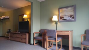 A hotel room with a television, two chairs, a wooden dresser, and a painting on the wall. - Harbor Lights Lodge (Kewaunee)