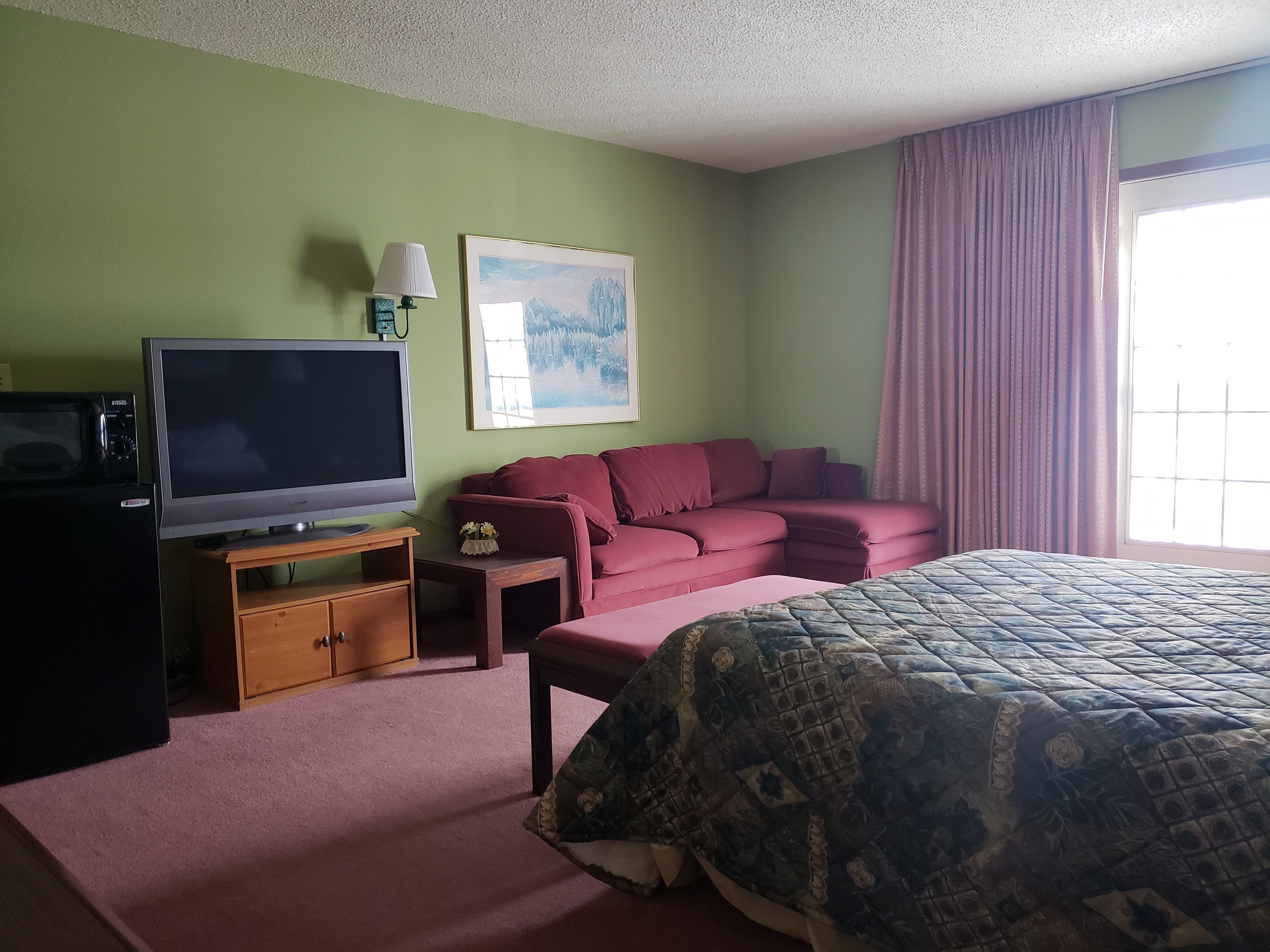 Una habitación de hotel con cama, televisor, sofá y una mesita.