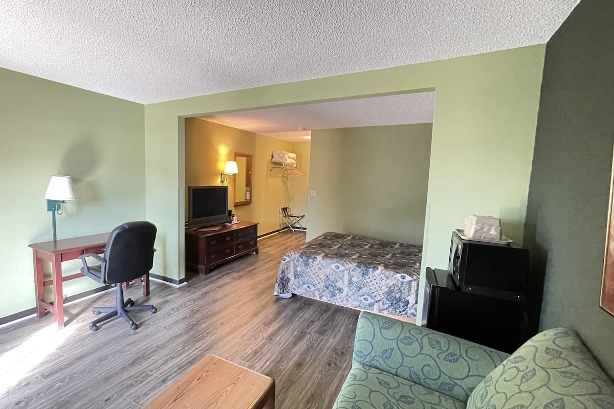 A compact hotel room with a bed, a desk, a chair, a television, and a microwave.
