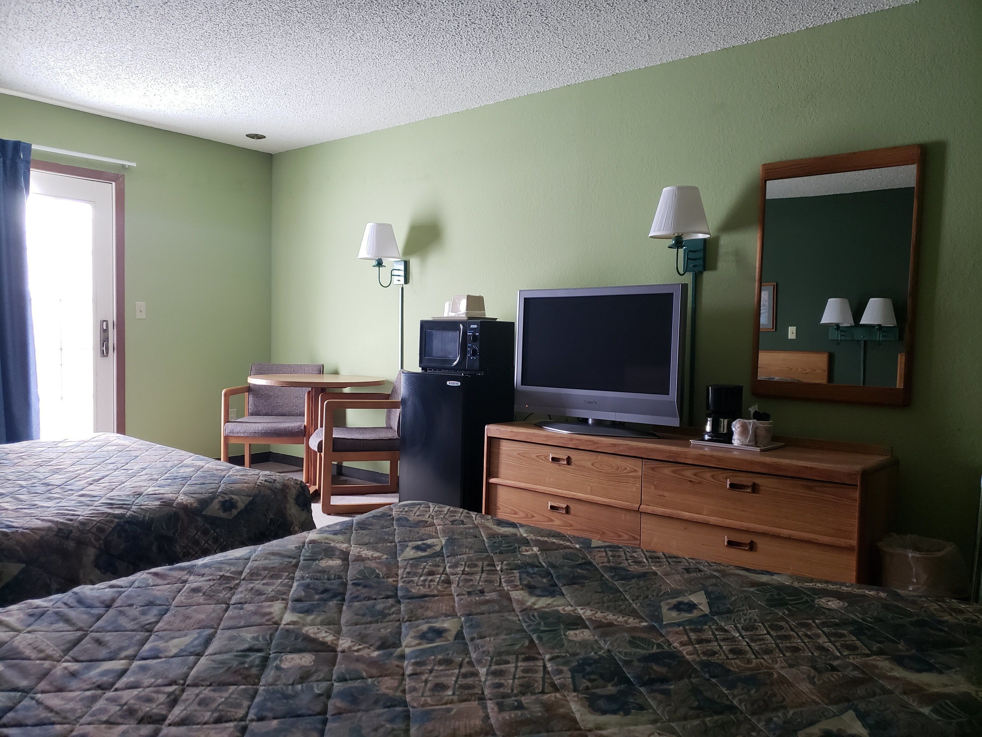 A hotel room with two beds, a small table with chairs, a television, a refrigerator, and a mirror.