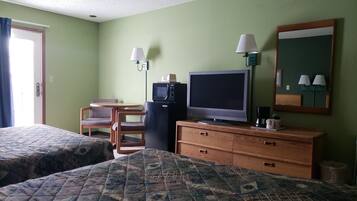 A hotel room with two beds, a small table with chairs, a television, a refrigerator, and a mirror.