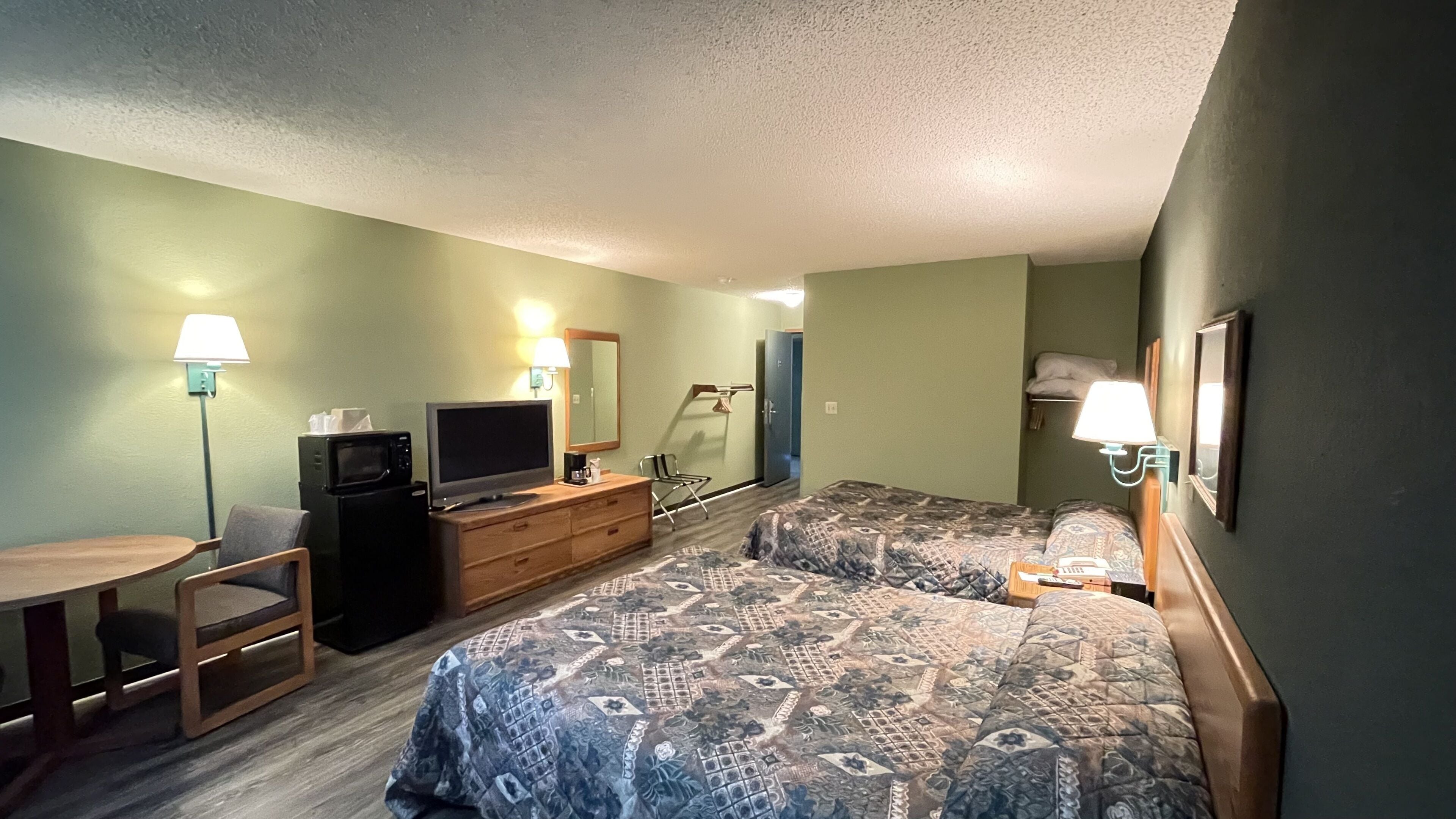 Ein Hotelzimmer mit zwei Betten, einem Schreibtisch, einem Fernseher, einer Mikrowelle und einem Sessel.