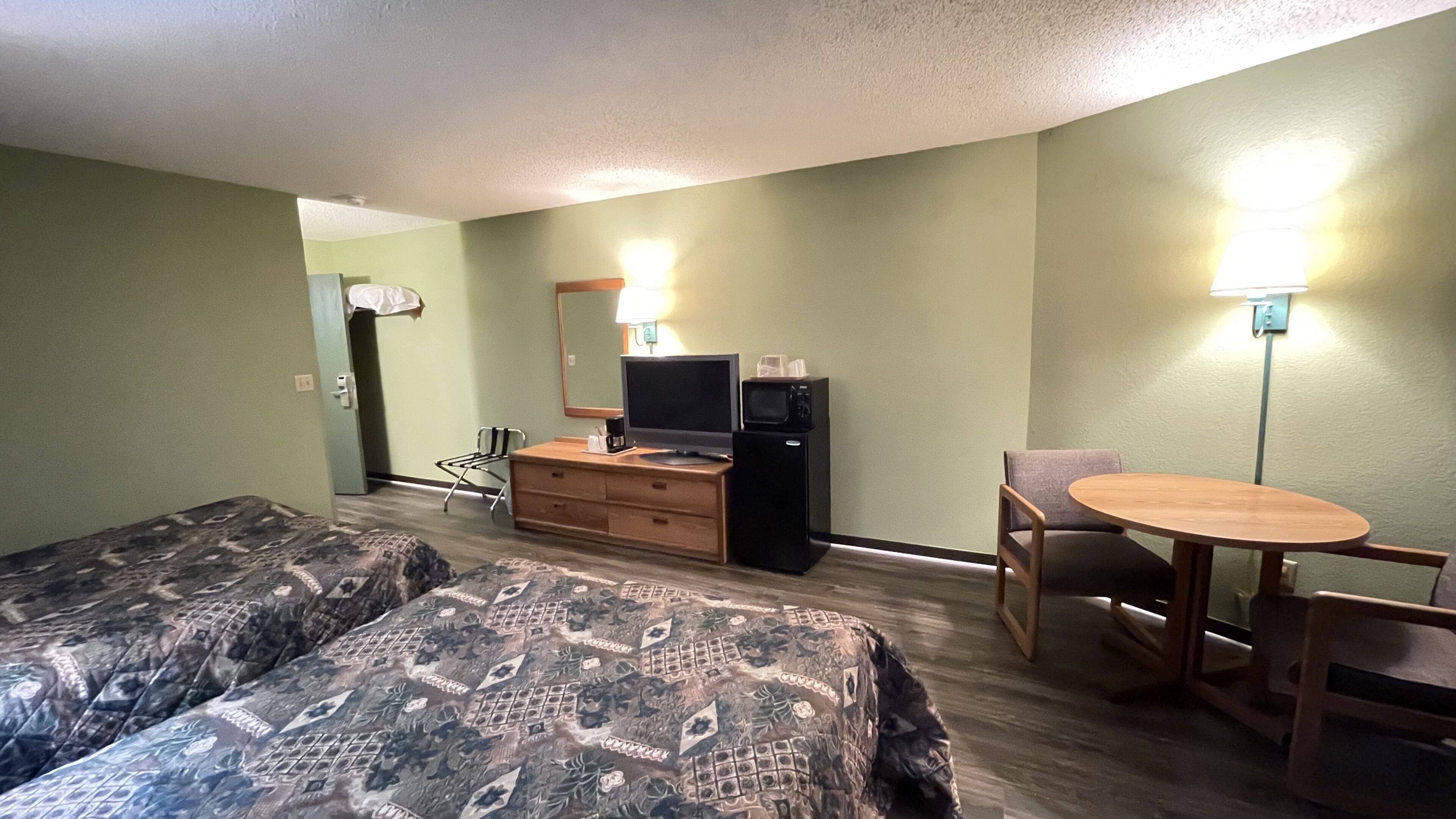 Habitación de hotel con dos camas, un escritorio con computadora, una silla, una mesita y un microondas.