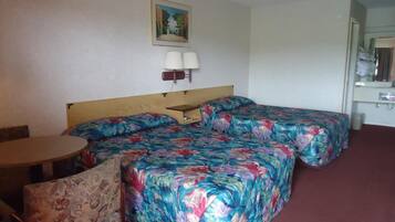 Quarto de hotel com cama de madeira, duas luminárias de cabeceira, uma mesinha e uma cadeira.