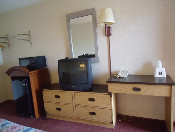 A hotel room with a wooden desk, a television, a lamp, a telephone, and a microwave. - Welborn Motel (Hamptonville)