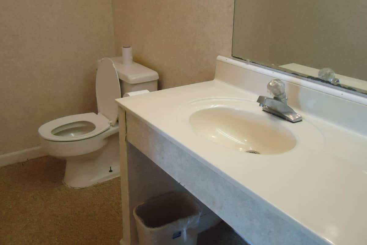 Une salle de bain avec des toilettes blanches, un lavabo et un miroir.