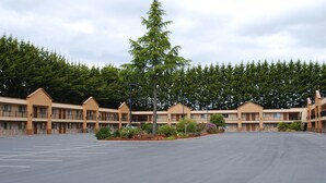 A motel with multiple buildings, a large parking lot, and a forested background. - McMinnville Inn (McMinnville)