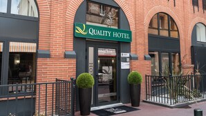 A brick building with a green sign that reads "Quality Hotel." There are two large potted plants in front of the entrance. - Quality Hotel Toulouse Centre (Toulouse)