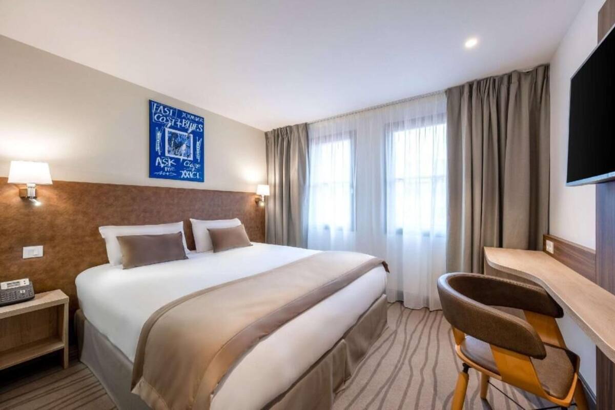 Habitación de hotel con una cama grande, un escritorio, una silla, un televisor de pantalla plana y un teléfono instalado en la pared.