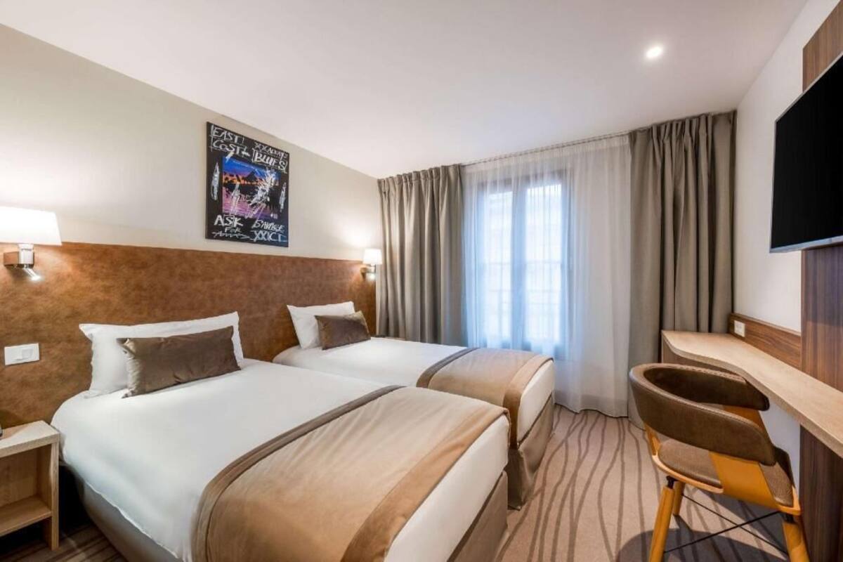 Habitación de hotel con dos camas, un escritorio, una silla, un televisor y un cartel en la pared.