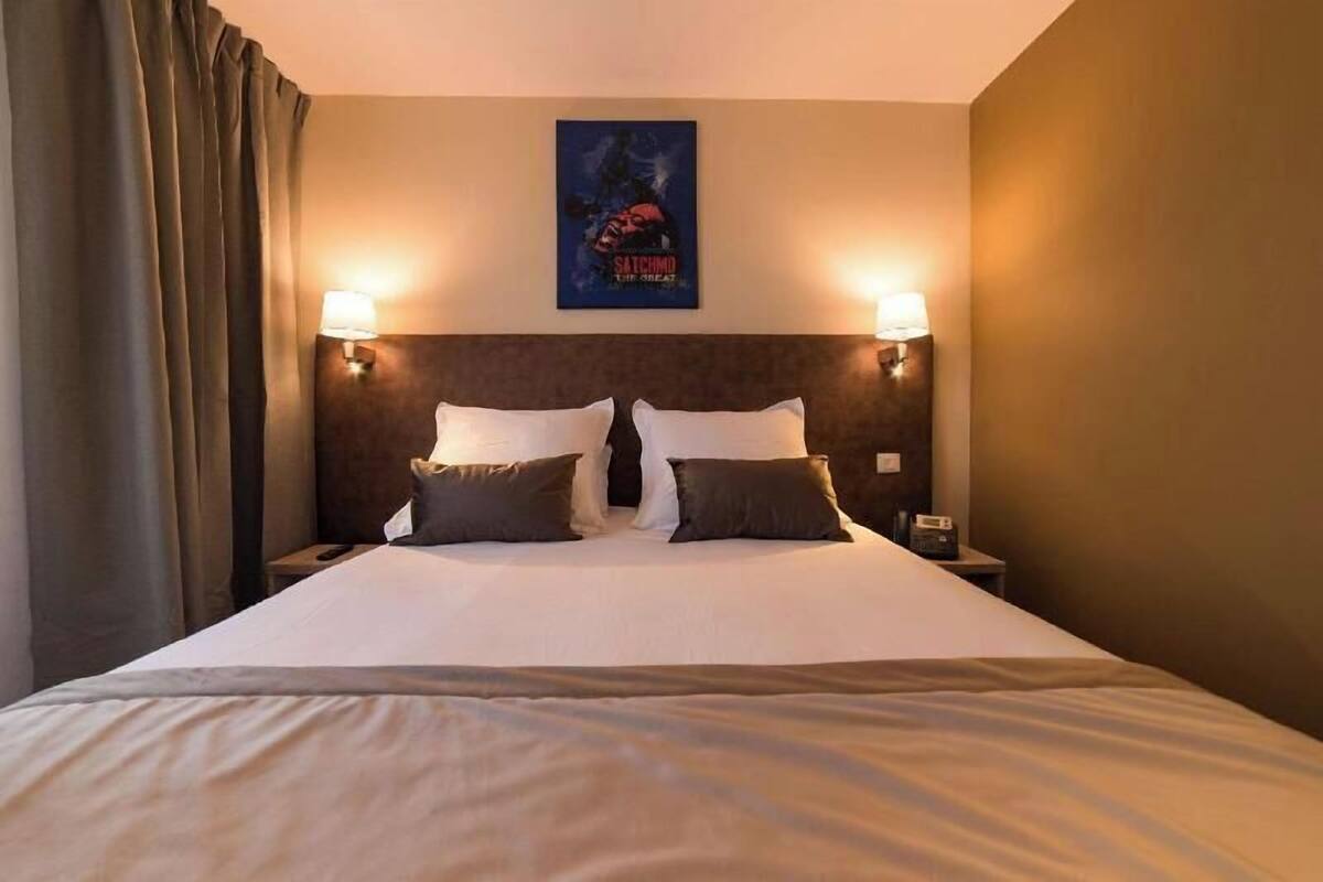 Habitación de hotel con una cama grande, dos lámparas de noche, un cartel en la pared y una mesita de noche con una radio.