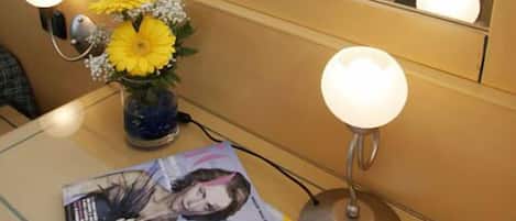 A hotel room with a bed, a bedside table with a lamp, a mirror, and a window.
