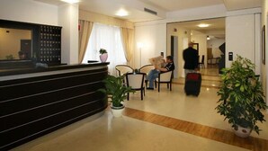 Un espace d’accueil d’hôtel comprenant un comptoir de réception, un coin salon et un couloir menant aux autres chambres.