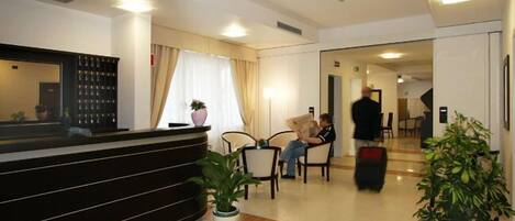 A hotel reception area with a reception desk, seating area, and a hallway leading to other rooms.