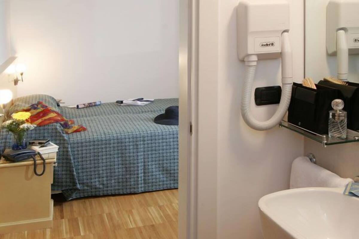 A hotel room with a bed, bedside table, lamp, and a bathroom with a sink and mirror.