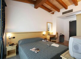 Camera d'albergo con un letto, comodini, una scrivania con lampada, uno specchio, un armadio e una televisione.