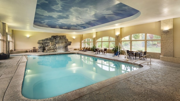 An indoor swimming pool with a stone wall and a ceiling mural of clouds. - Zermatt Utah Resort & Spa Trademark Collection by Wyndham (Midway)