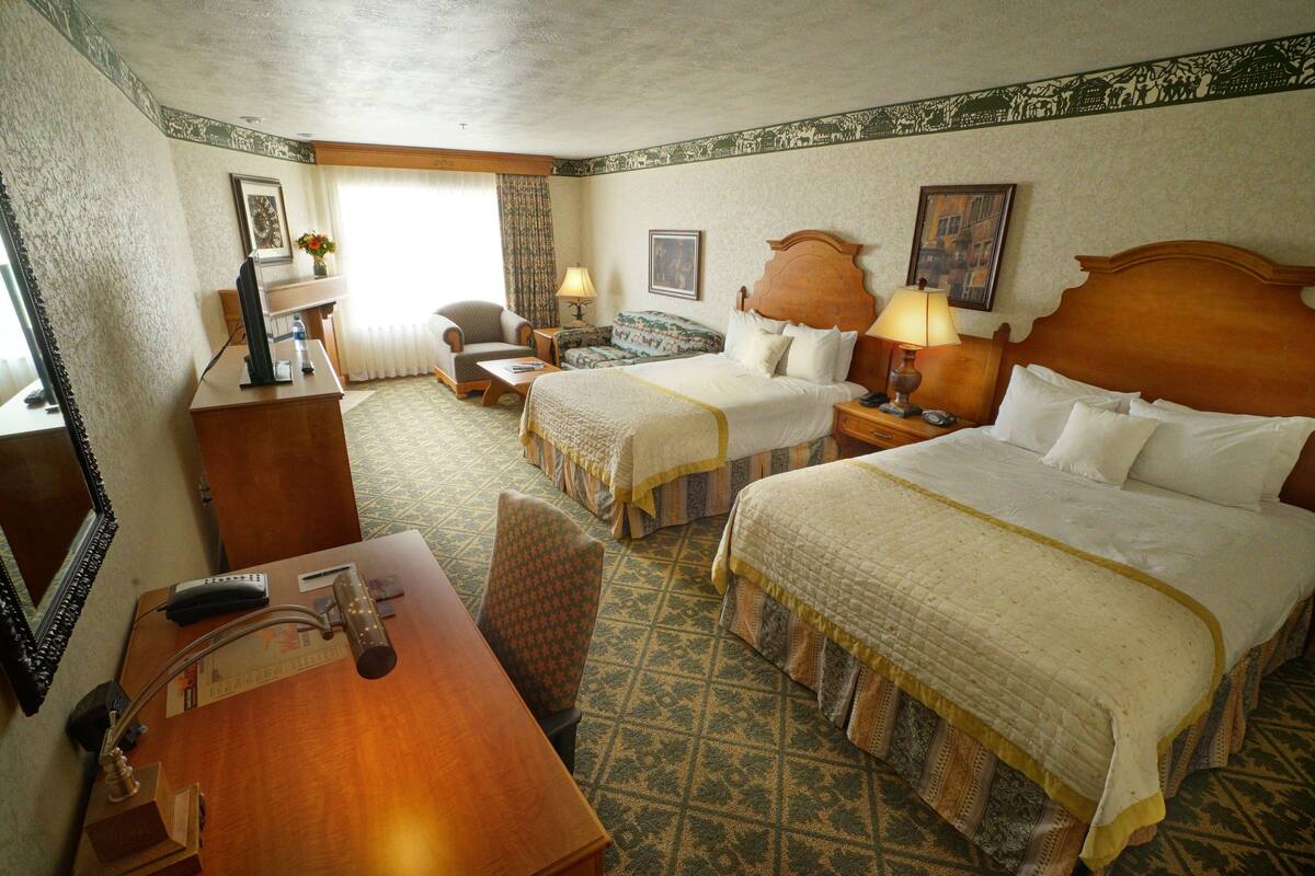 A hotel room with two beds, a desk with a chair, a small table, and a mirror.