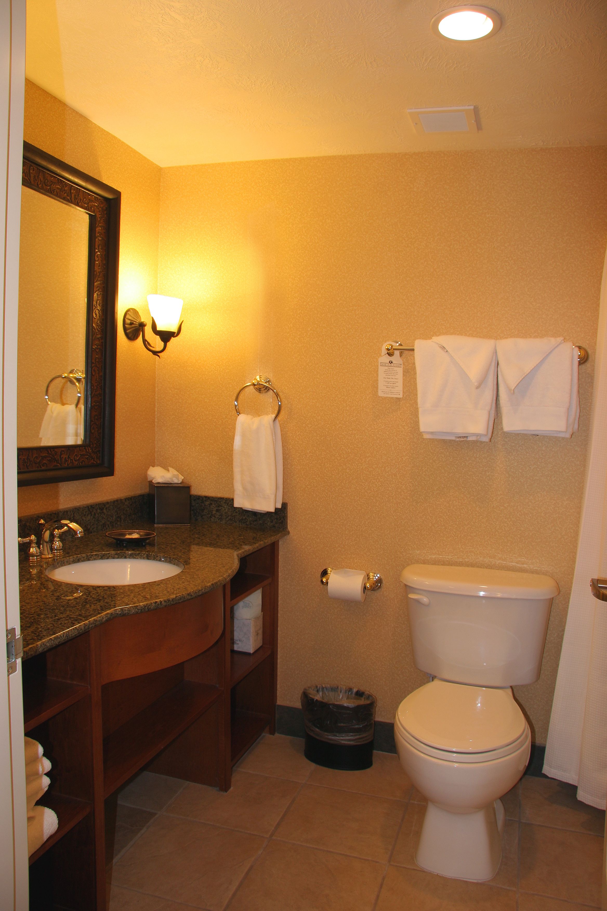 A bathroom with a sink, mirror, towel rack, toilet, and trash can.