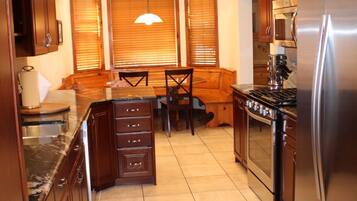 A kitchen with wooden cabinets, a stainless steel refrigerator, a built-in oven, and a dining area with a bench and chairs.