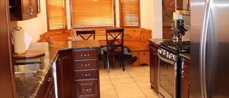 A kitchen with wooden cabinets, a stainless steel refrigerator, a built-in oven, and a dining area with a bench and chairs.