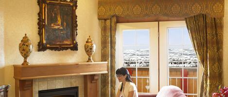 A cozy room with a fireplace, a large window with curtains, and a painting on the wall.